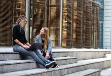 Exploring Your Options For A Home Away From Home in Australia Two women sitting on steps with a laptop, discussing ideas in urban setting.