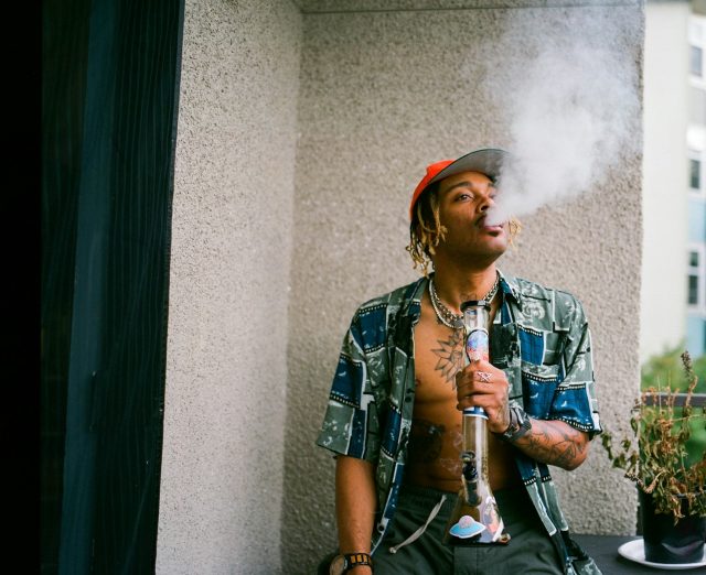Photo by LexScope a man smoking a cigarette next to a potted plant
